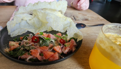 A plate of fresh salad with herbs and chili, topped with crispy crackers, alongside a glass of yellow drink.