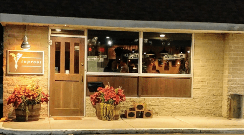 Exterior of a restaurant named "taproot," featuring a wooden door, large windows, and potted plants in front.