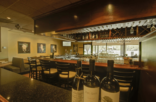 A cozy bar area with a polished countertop, wine bottles, and framed artwork on the walls. Bright and inviting atmosphere.