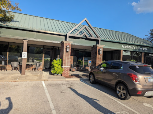 Exterior of Garozzo's Ristorante with a green roof, brick facade, and outdoor seating area. A car is parked in front.