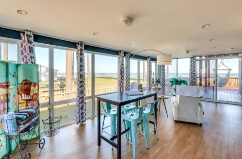 Bright, modern living space with large windows, a dining table, and coastal decor overlooking a scenic view.