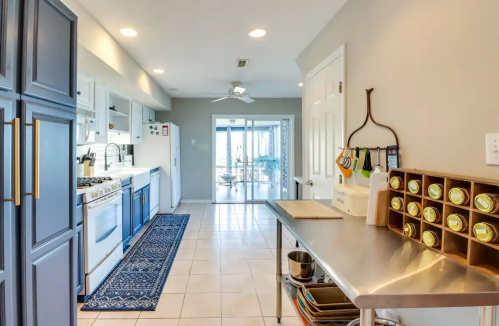 Bright kitchen with blue cabinets, stainless steel countertops, and a view of a sunlit dining area through sliding doors.