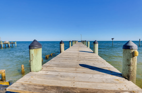 A wooden pier extends into calm blue waters under a clear blue sky.