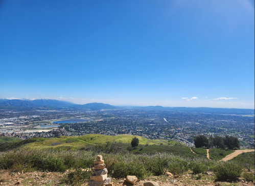 A scenic view from a hilltop overlooking a valley, with stacked stones in the foreground and clear blue skies.