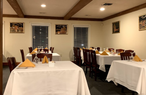 A cozy restaurant interior with neatly set tables, white tablecloths, and decorative wall art.