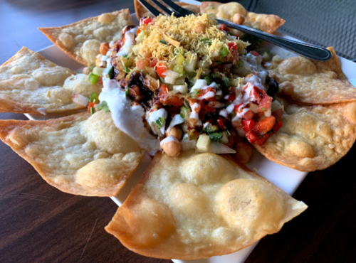 A plate of crispy tortilla chips topped with a colorful mix of vegetables, yogurt, and spices.