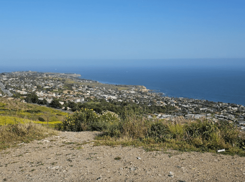 A scenic view of a coastal town with greenery, hills, and the ocean under a clear blue sky.