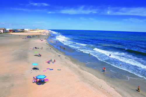 A sunny beach scene with people enjoying the water, colorful umbrellas, and a clear blue sky.
