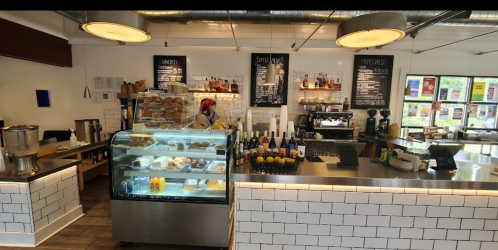 A cozy café interior featuring a display case with pastries, a coffee counter, and a barista at work.