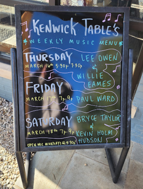 Chalkboard sign listing Kenwick Table's weekly music menu for March, featuring artists and performance times.