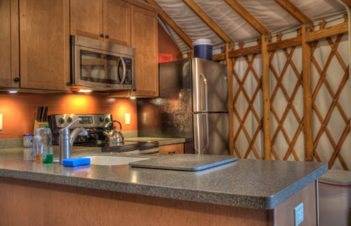 Cozy kitchen inside a yurt, featuring wooden cabinets, stainless steel appliances, and a countertop with a sink.