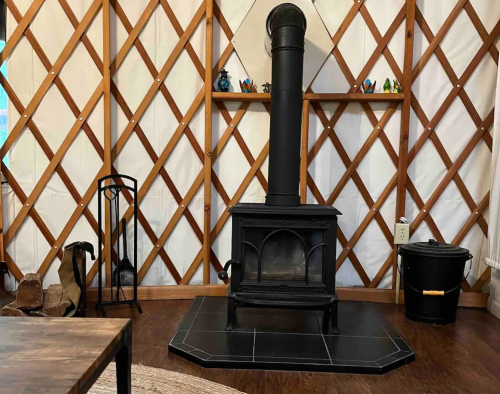 A cozy yurt interior featuring a black wood stove, wooden shelves, and a rustic wooden floor.