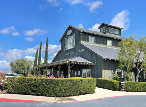 A charming green building with a sign reading "Tasting Room," surrounded by neatly trimmed hedges and tall trees.