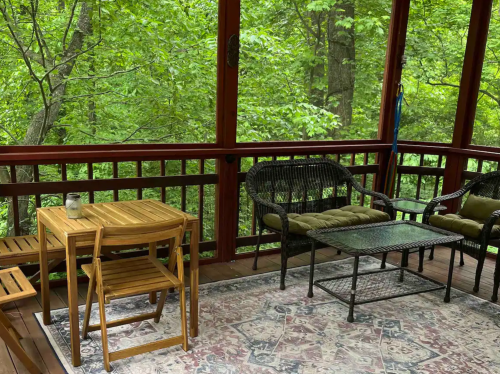 A cozy screened porch with wooden furniture and a view of lush green trees outside.