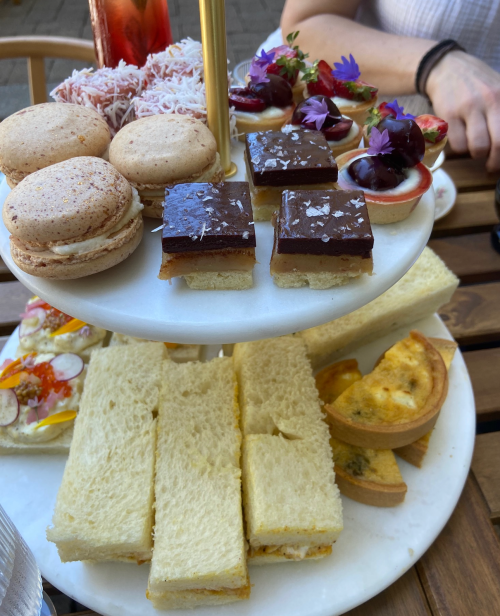 A tiered dessert stand featuring macarons, chocolate squares, mini tarts, and assorted sandwiches.