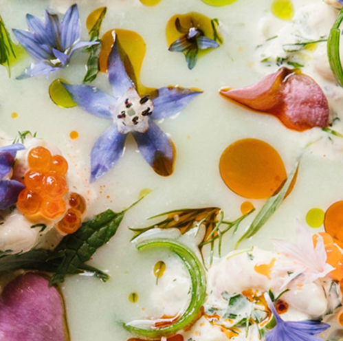 A vibrant dish featuring a creamy base, adorned with edible flowers, herbs, and colorful garnishes.