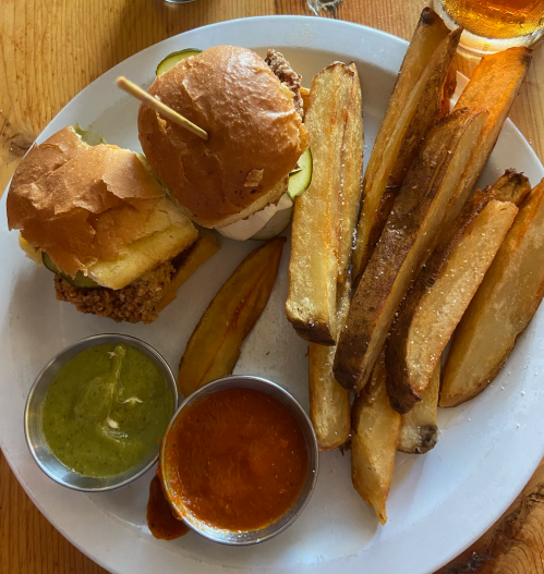 A plate with two sliders, pickles, and a side of crispy fries with green and orange dipping sauces.