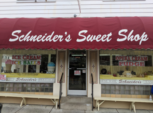 A storefront with a red awning reading "Schneider's Sweet Shop," featuring ice cream and fudge displays in the windows.