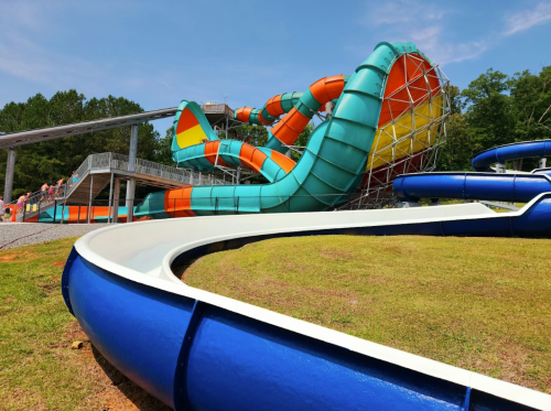 A colorful water slide complex with twisting slides and a large funnel, surrounded by green grass and trees.