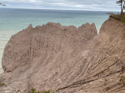 A rugged cliffside overlooking a calm lake, with layered rock formations and a cloudy sky above.