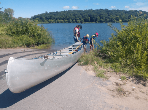 A group of people near a canoe by a lake, preparing to explore the water on a sunny day.