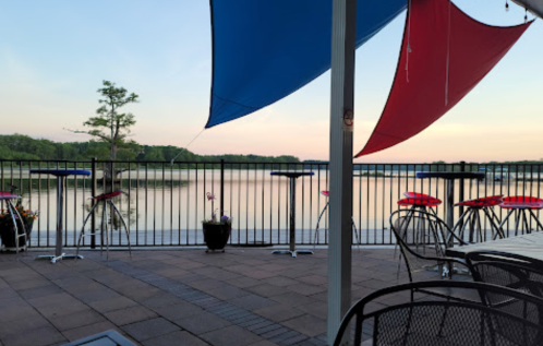 A serene lakeside view at sunset, featuring colorful sails and outdoor seating on a patio.