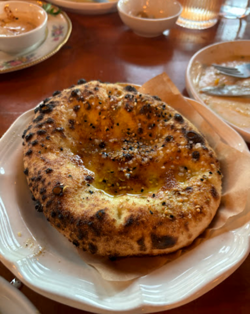 A freshly baked, golden-brown naan bread with a slightly charred surface, served on a white plate.