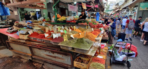 A vibrant market stall filled with colorful spices, fruits, and vegetables, bustling with shoppers.
