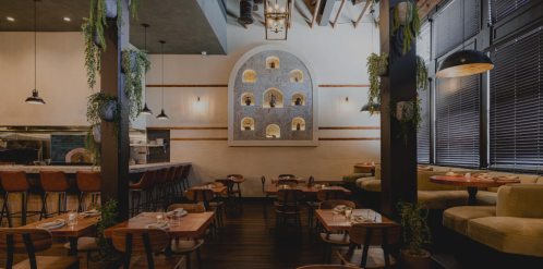 Interior of a modern restaurant featuring wooden tables, a bar, and decorative wall niches with plants.