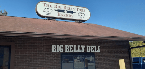 Sign for "The Big Belly Deli & Bakery" on a brick building with a clear view of the entrance.