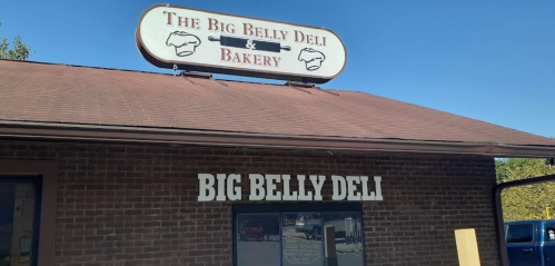 Sign for "The Big Belly Deli & Bakery" on a brick building with a clear view of the entrance.