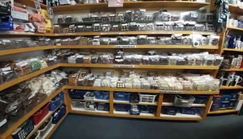 A well-stocked candy shop with shelves of assorted chocolates in clear bags, labeled by type: dark, milk, and white.
