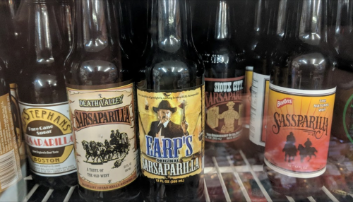 A variety of sarsaparilla soda bottles displayed in a cooler, featuring different labels and designs.