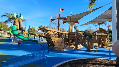 A colorful playground featuring a pirate ship structure, slides, and climbing areas under a clear blue sky.