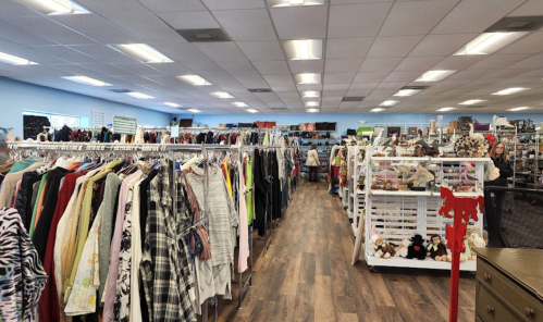 A spacious thrift store aisle lined with racks of clothing and shelves of various items, brightly lit and organized.