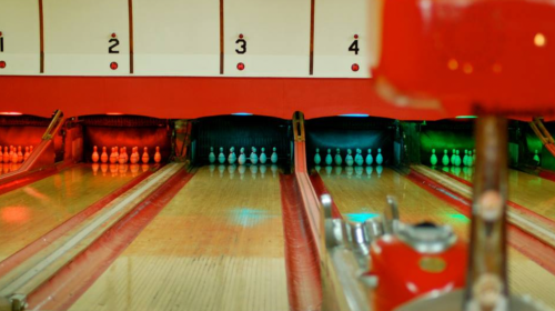 Bowling alley lanes with colorful lights and pins set up at the end, creating a vibrant atmosphere.