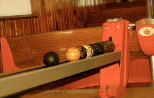 A close-up of a bowling ball return system with four bowling balls lined up on a metal track.