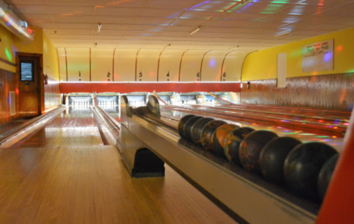 A bowling alley with colorful lights, featuring lanes and a rack of bowling balls in the foreground.