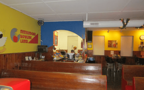 Interior of a bowling alley with colorful walls, wooden benches, and a snack counter in the background.