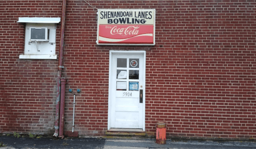 Entrance to Shenandoah Lanes Bowling, featuring a Coca-Cola sign, on a brick wall. Address: 5904.