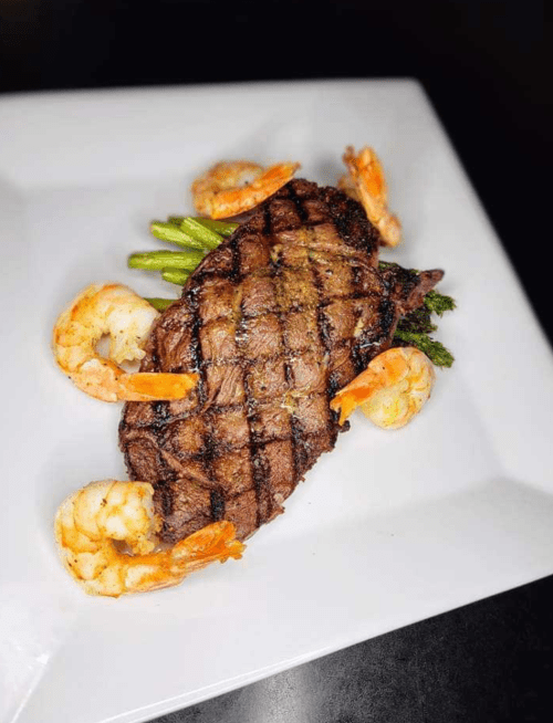 Grilled steak with shrimp and asparagus, presented on a white plate.