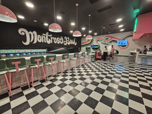 A retro-style bowling alley with pink and green decor, checkered floor, and a vibrant mural on the wall.