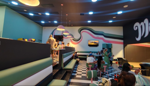 A vibrant diner interior with colorful decor, checkered floors, and patrons enjoying their time at booths and counters.