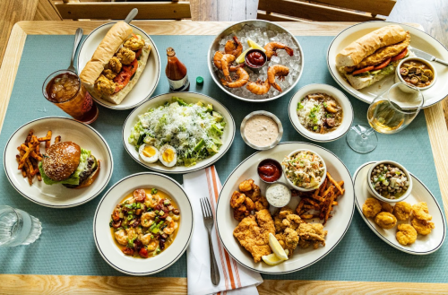 A spread of various dishes including fried chicken, shrimp, salads, burgers, and sweet potato fries on a table.
