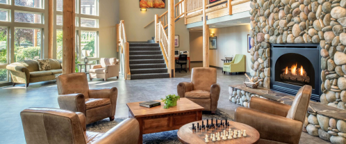 Cozy lobby with stone fireplace, wooden accents, seating area, and a chess set on a table. Stairs lead to upper level.