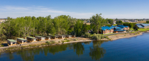 Aerial view of a lakeside resort with cabins and a main building surrounded by trees and clear blue water.