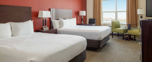 A hotel room featuring two beds, a window with a view, and modern furnishings in warm tones.