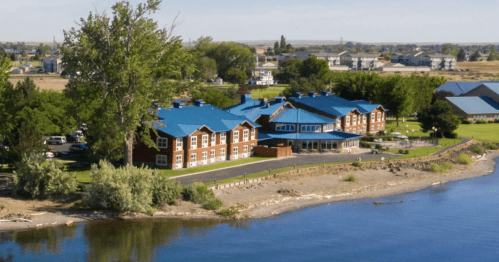 Aerial view of a lakeside resort with cabins and a main building surrounded by trees and clear blue water.
