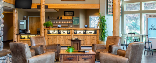 Cozy lobby with wooden decor, comfortable chairs, a coffee bar, and large windows letting in natural light.