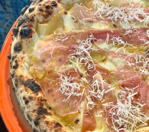 Close-up of a pizza topped with thin slices of ham and shredded cheese on a charred crust.